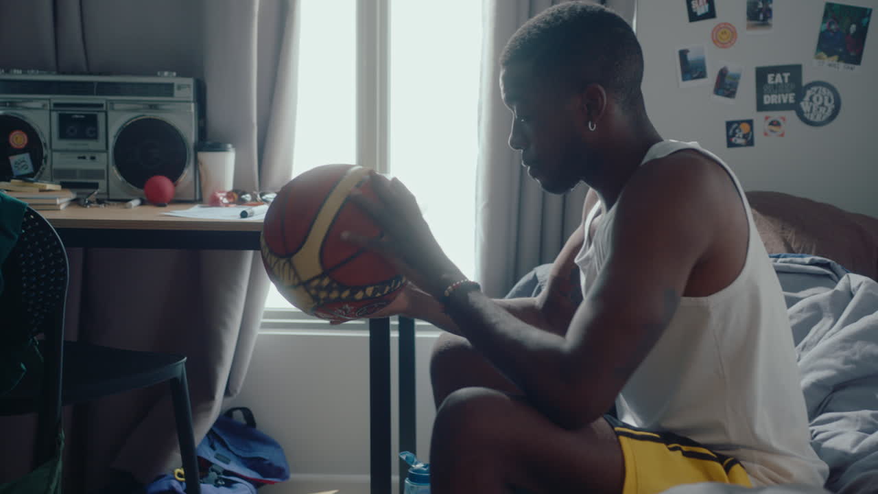 Young Black Basketballer Sitting in Bedroom Playing with a Ball