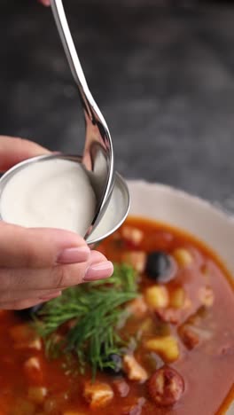 sirviendo sopa de solyanka con crema agria