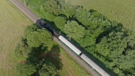 aerial view of a train traveling through green fields and forests with solar panels