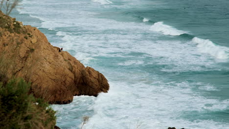 Fishermen-angling-from-rocks-in-Kogel-Bay,-waves-roll-in-on-windy-day