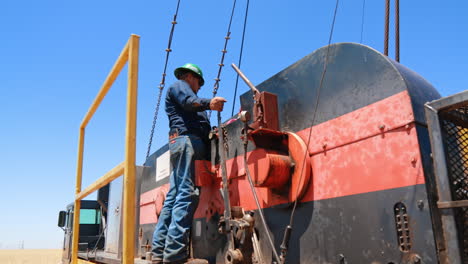 metal tower reflecting bright sun. low angle view at the derrick with attached wires stretching to the truck where a male worker stands.