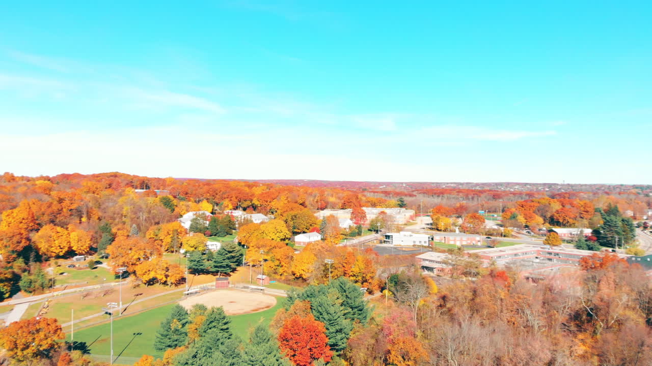 4K Drone Footage the colors of fall, big red and orange leaves as far as the eye can see from a birds eye-view, we see the distant baseball field as we pan across the horizon