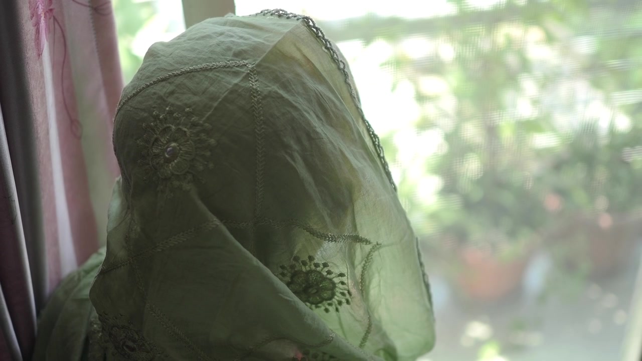 Mulher usando lenço de cabeça verde tradicional olhando pela janela
