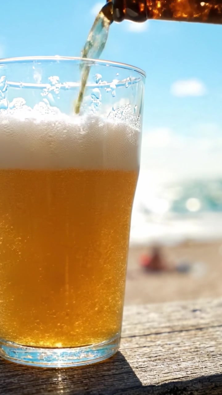 Bevanda rinfrescante in un contesto di spiaggia soleggiata: una vista ravvicinata di un bicchiere di birra con bollicine e schiuma, perfetto per il relax e il piacere durante il clima caldo
