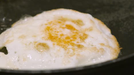 fried egg flipping over in hot pan as it slides across the pan in bubbling hot oil. cooking protein rich breakfast healthy food