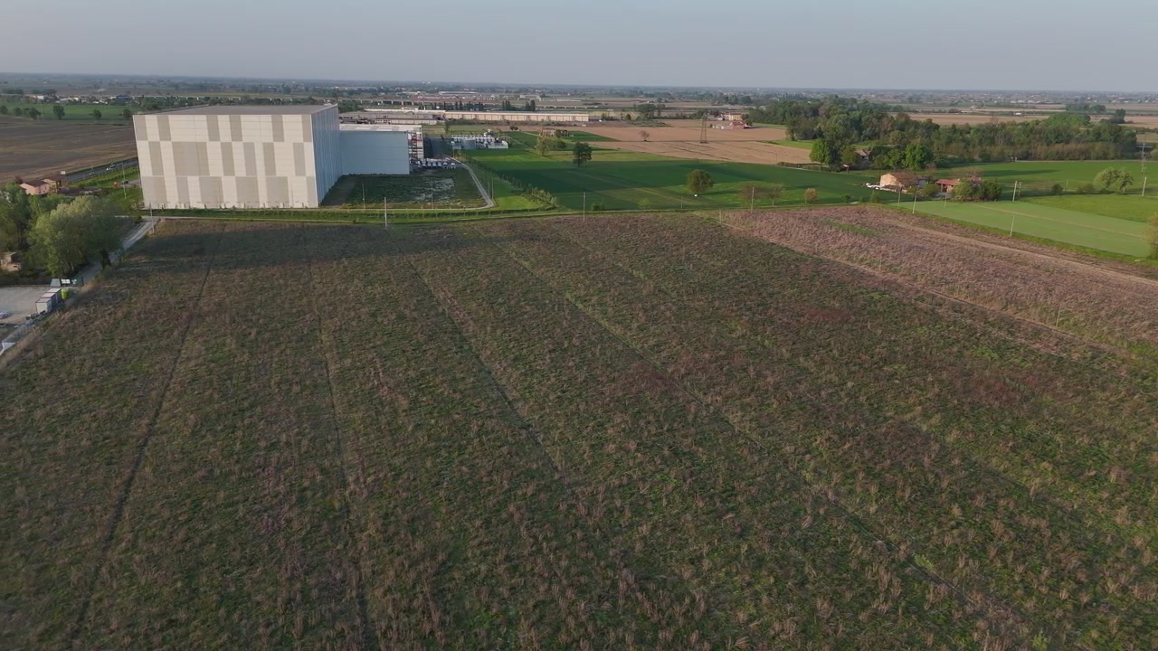 Magazzino frigorifero automatizzato vicino alla SP426R Barabasca Fiorenzuola d'Arda con adiacente costruzione di un impianto solare fotovoltaico, strade di servizio e terreni agricoli circostanti, ampia ripresa aerea, nella Pianura Padana.