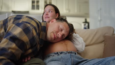de cerca feliz hombre de mediana edad se apoya en el vientre de su esposa embarazada para escuchar a su bebé en casa