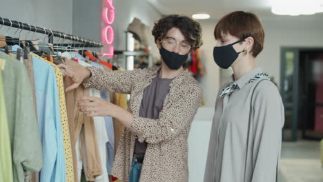 stylist in face mask helping female customer in clothes shop