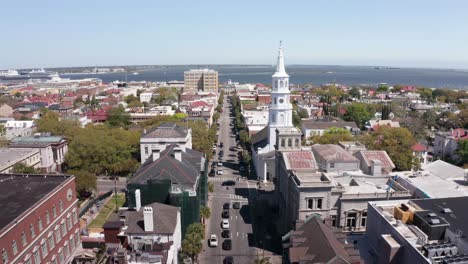 Toma-Aérea-Baja-Volando-Por-Una-Calle-Ancha-Hacia-El-Puerto-En-El-Histórico-Barrio-Francés-De-Charleston,-Carolina-Del-Sur.