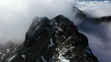 Drone-shot-of-the-dark-and-black-peak-of-the-mountain-Pico-Ruivo-in-Madeira-with-thin-clouds-flying-around