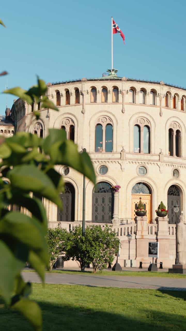 Vertical sunny exterior of Stortinget Parliament’s circular chamber, Norway flag waving above, bright clear day, iconic Oslo architecture