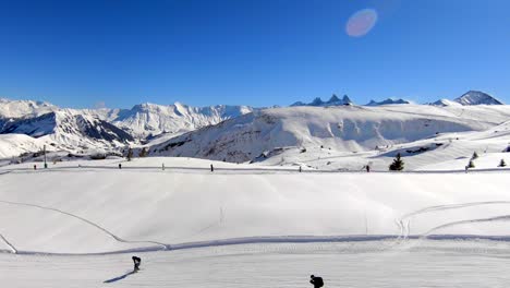 Aerial-shot-moving-over-a-tow-lift-and-a-ski-piste-in-a-snowy-wintersport-area,-with-distant-mountain-peaks-in-the-background