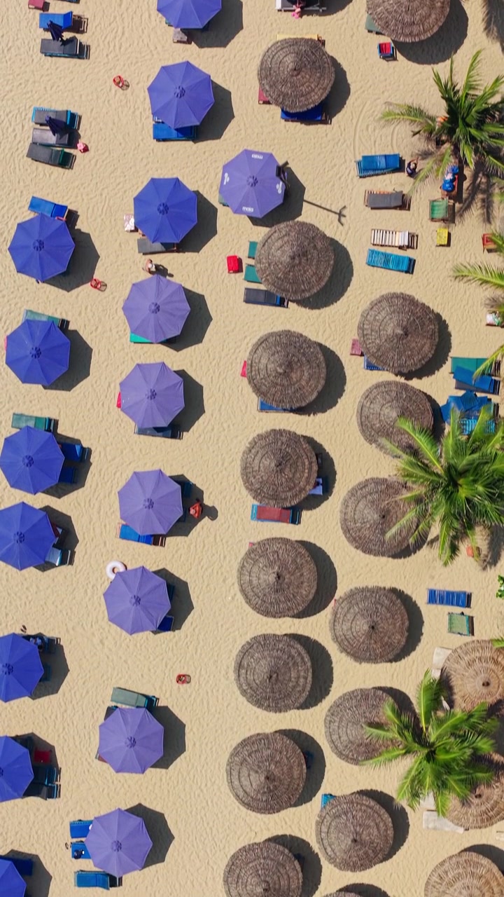 Ombrelloni da spiaggia costeggiano la riva sabbiosa di My Khe Beach a Da Nang, Vietnam - drone, scatto verticale