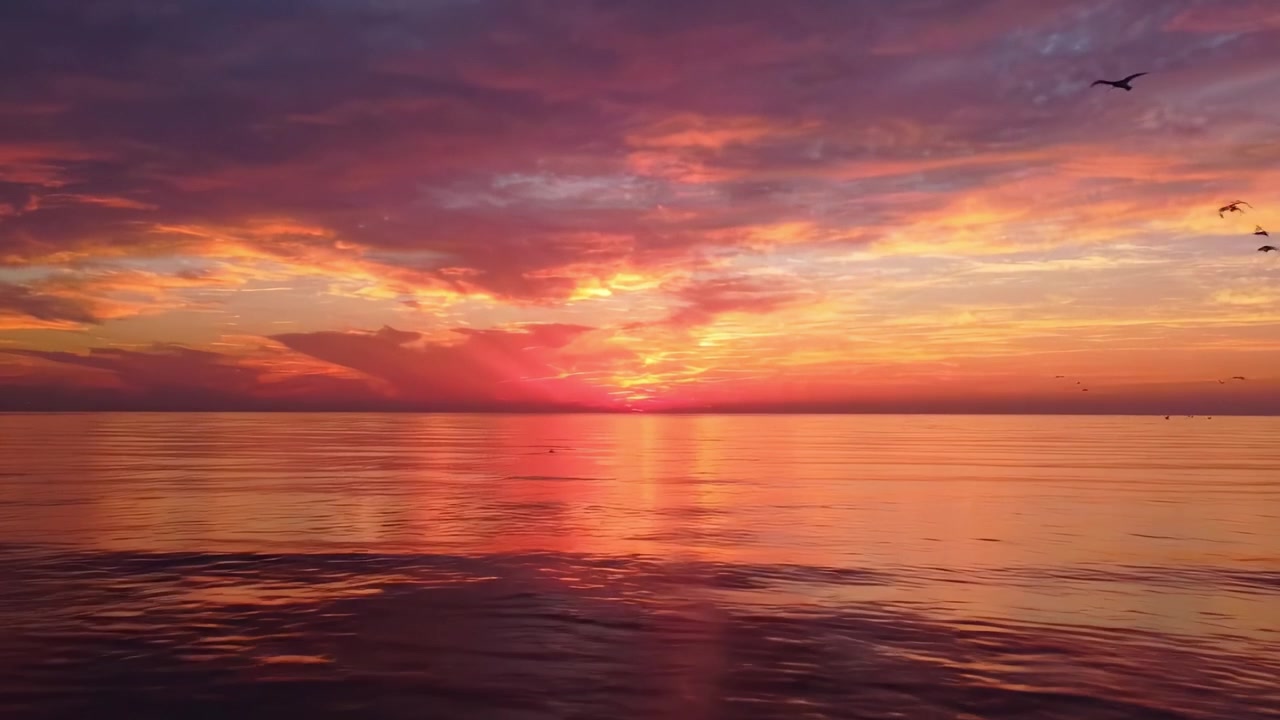 Matahari Terbenam yang Indah di Atas Laut Tenang, Menerangi Langit dengan Warna-warna Cerah dan Memantul di Permukaan Air yang Tenang Saat Senja