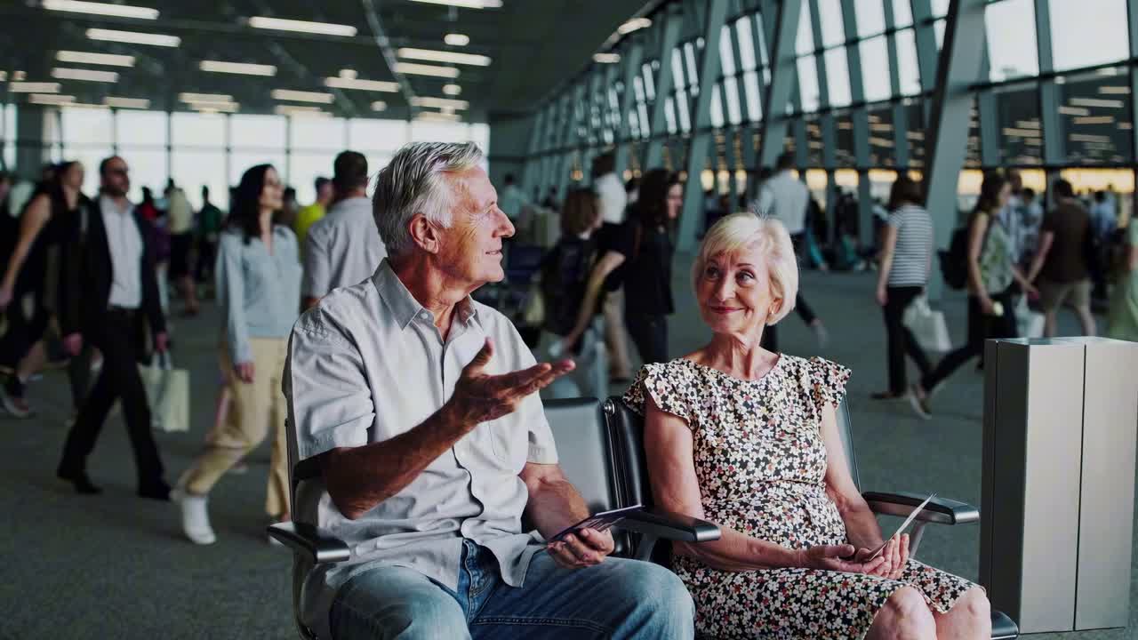 A candid video captures an elderly couple at an airport, seated and conversing