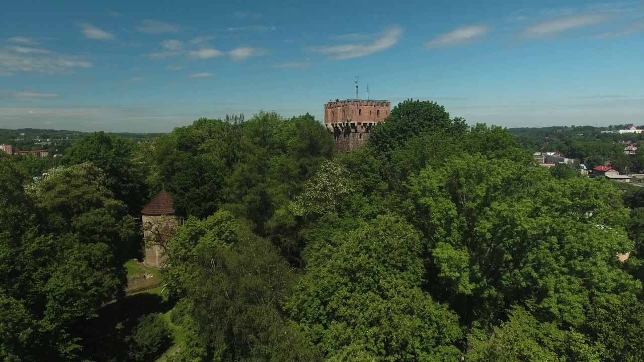 una torre medieval histórica y restaurada situada en el corazón de un gran parque lleno de árboles verdes exuberantes durante el verano en polonia, capturada en una dinámica toma de dron 4k