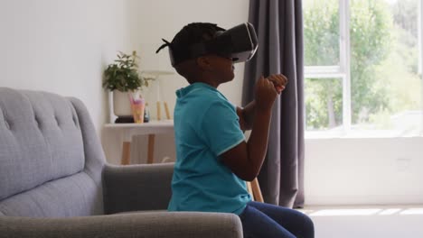 Afroamerikanischer-Junge-Gestikuliert,-Während-Er-Zu-Hause-Auf-Der-Couch-Sitzt-Und-Ein-VR-Headset-Benutzt