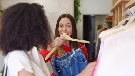 dos amigas comprando en una tienda de ropa eligiendo vaqueros de un estante