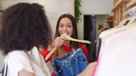 two female friends shopping in clothing store choosing jeans from rack