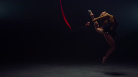 pretty gymnast jumping flying ribbon indoors. flexible girl rehearsing inside.