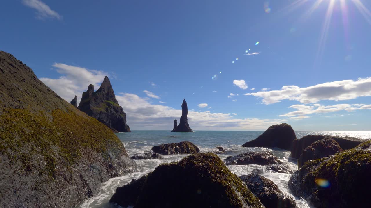 las olas chocan contra las rocas de musgo en la famosa playa negra de islandia, torres en el océano, zoom suave en