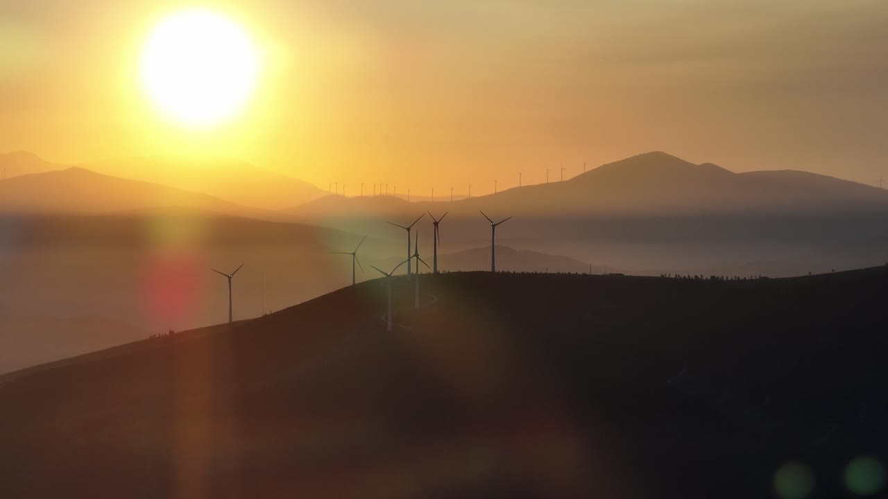 Multiple wind turbines at sunrise standing on a hill.