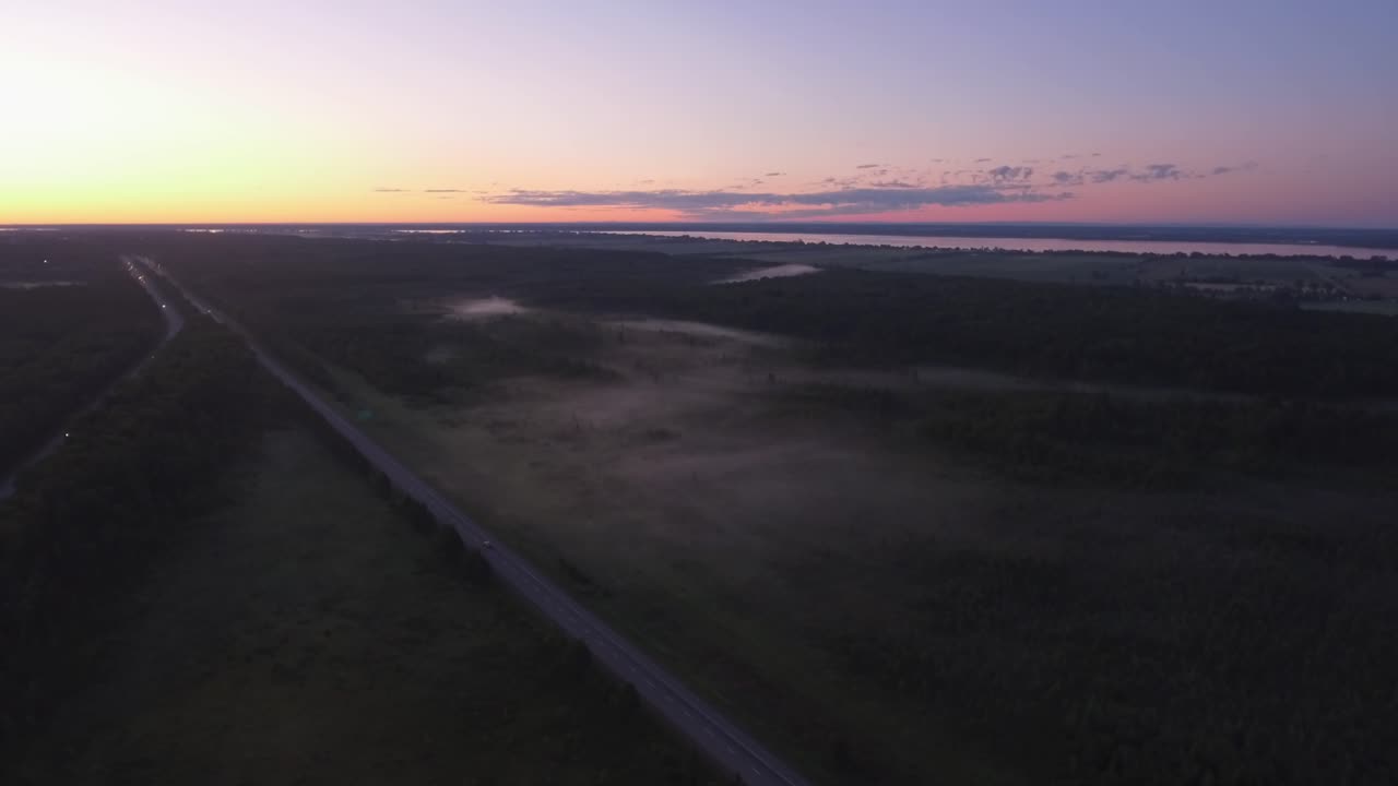 Late evening sunset drone shot w over the highway with low lying fog cover the trees