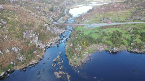 wide panning aerial shot of gap of dunloe, bearna or choimín, mountain pass in county kerry, ireland, with a bridge over the river loe