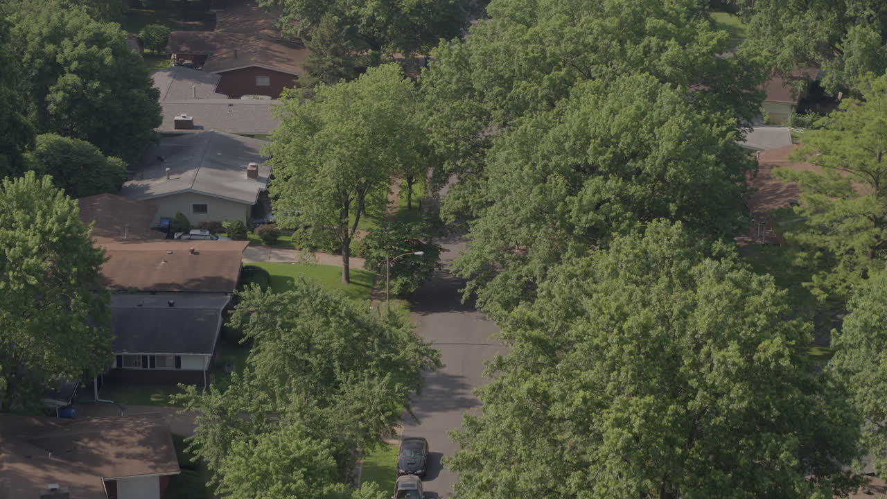 Aerial pull down an old suburban street with houses, trees, driveways, street and cars