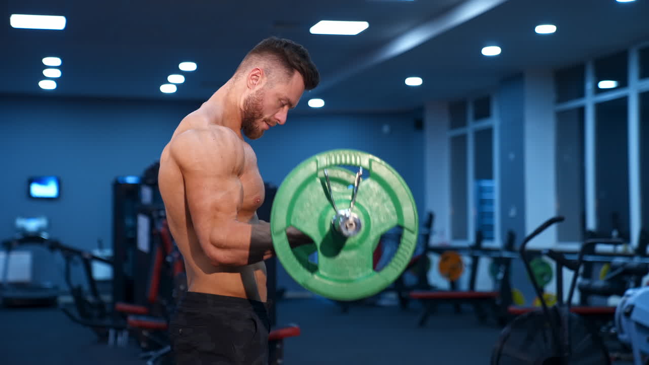 Muscular athlete doing exercise with barbell. Strong man working out arm muscles. Bodybuilding shoulder exercise in a gym.