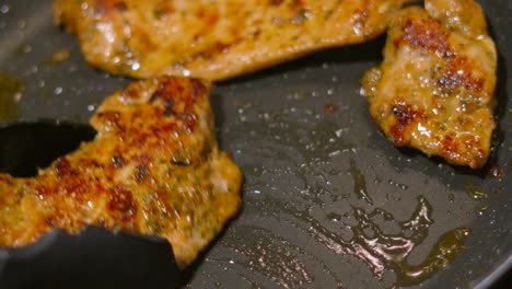 chef using tongs to move chinese flavoured chicken steak fillets around hot frying pan. food photography footage 4k.