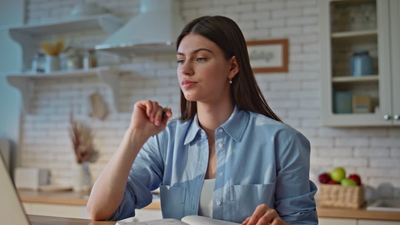 Girl freelancer making notes in notepad looking laptop screen indoors closeup