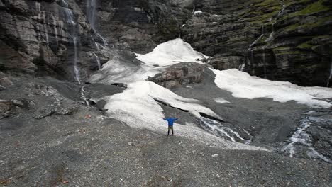 Man-victory-sign-at-amazing-spot-with-snow-and-waterfalls,-challenging-goal-done