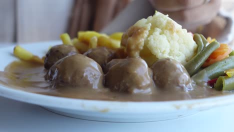 person eating meatballs with gravy, cauliflower, and green beans