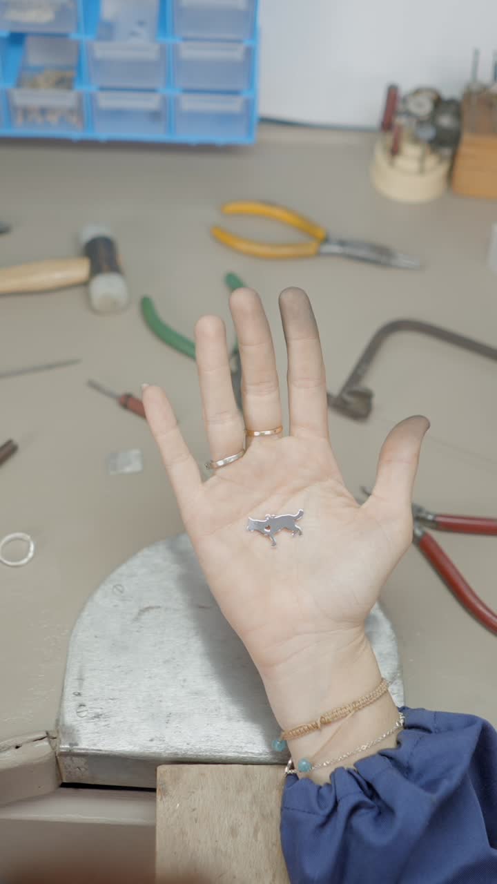 Hand holding a dog-shaped metal charm in a jewelry workshop