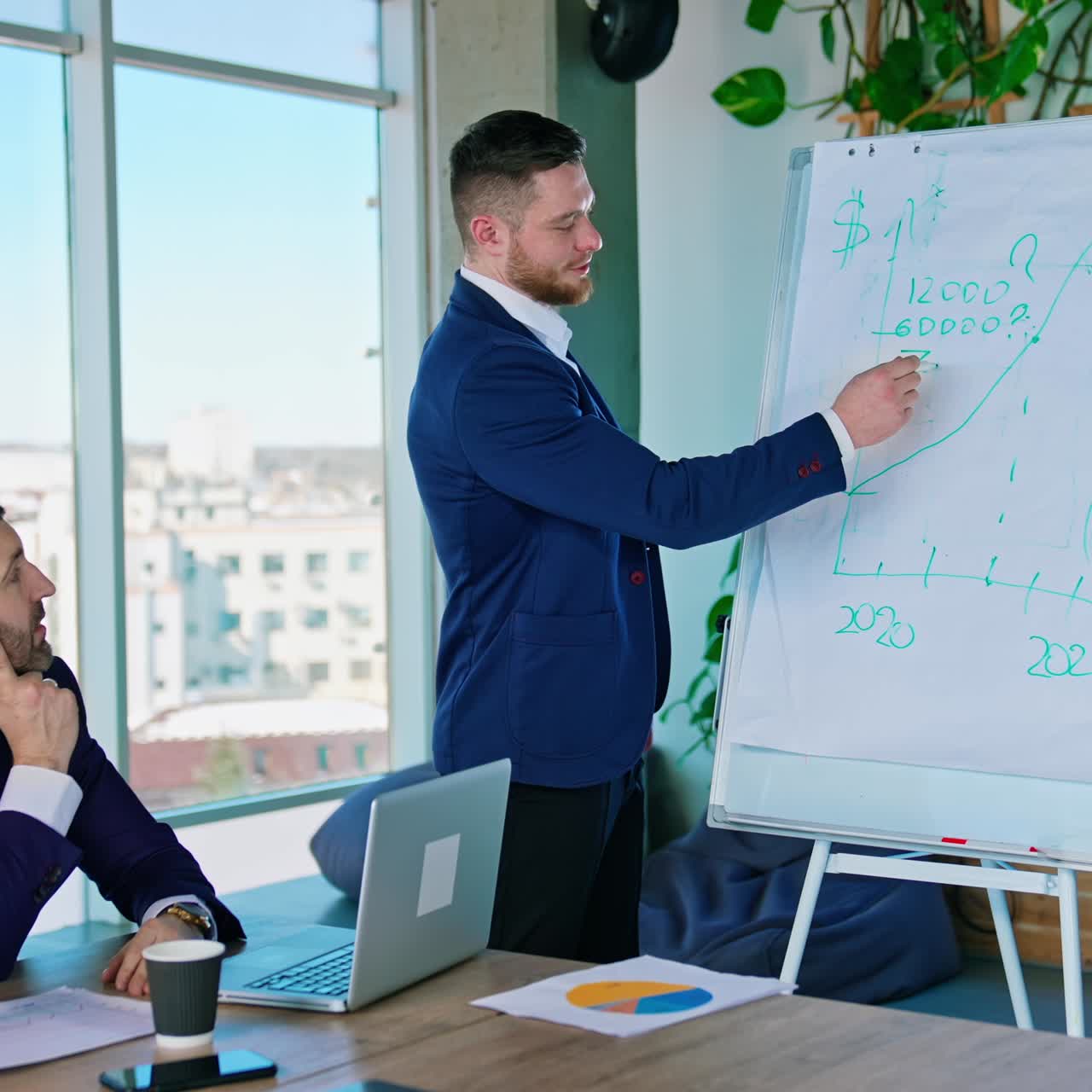 Young male entrepreneur talking about new strategy of a project. Businessman writing on a board with a marker and explains to his business coworkers in office