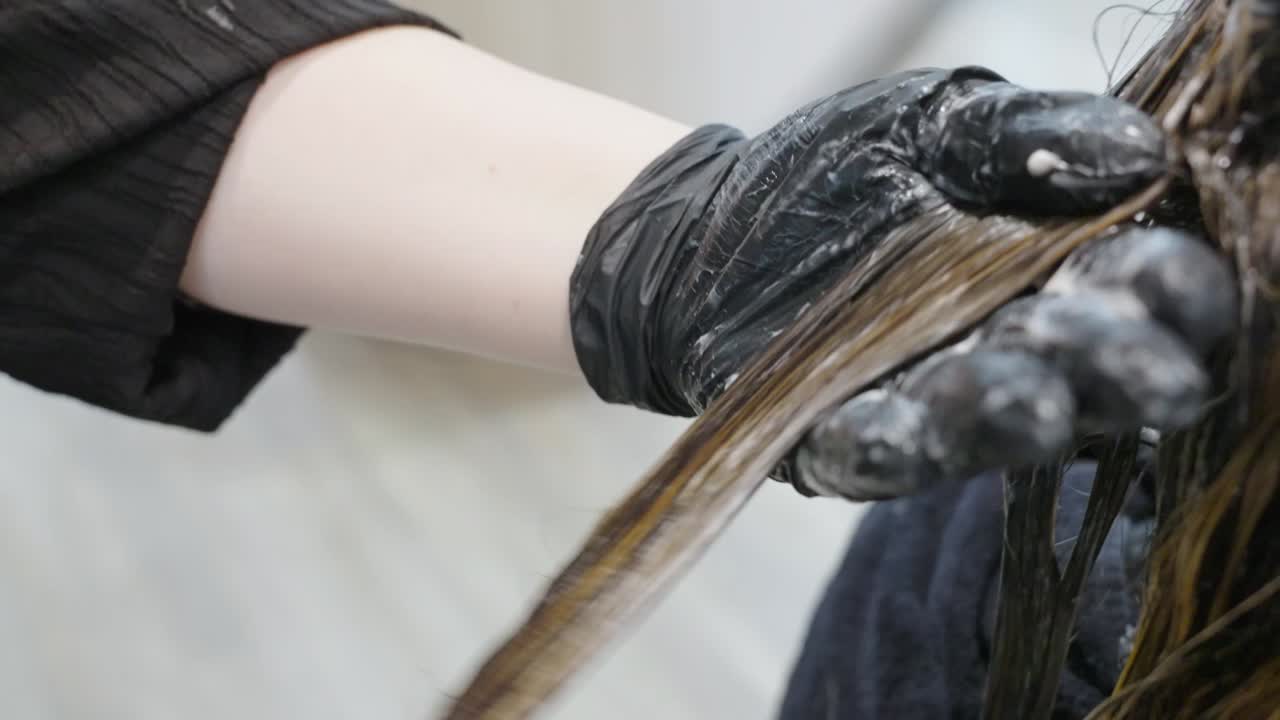 A hairstylist applies bleach paste on a layer of a woman's hair at a salon