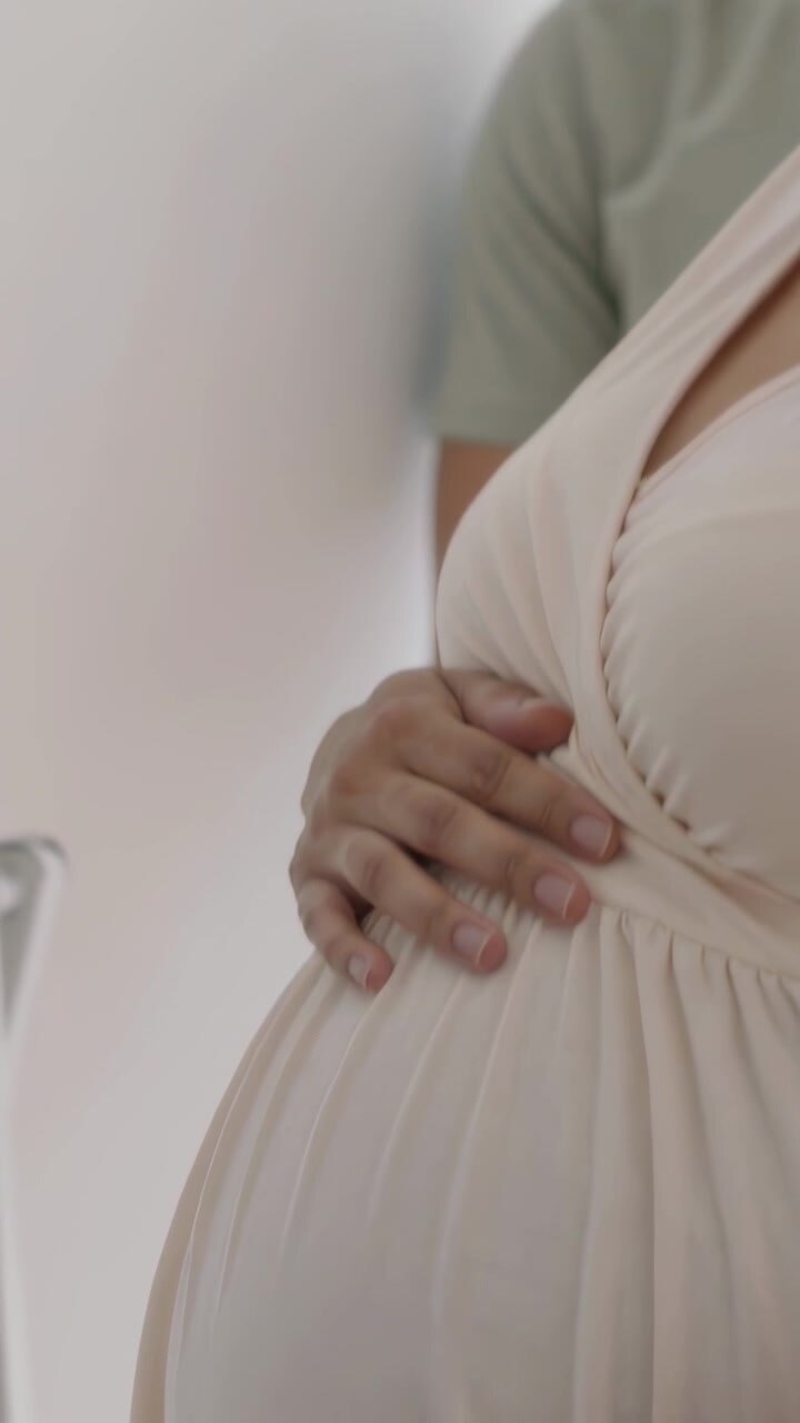 Video verticale: Donna sorridente in abito premaman che accarezza la pancia per creare un legame a casa con il partner.