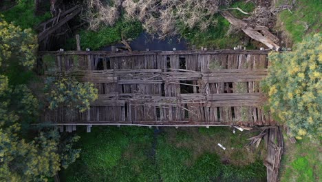 drone top down over old wooden bridge in bad condition over a beautiful waterway running between