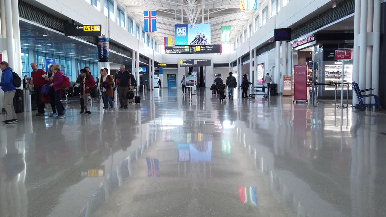 People in line begin boarding their flight from a terminal at Dulles International Airport near Washington, D.C.  Bright sunlight and modern white interior of airport. Travellers get on airplane.