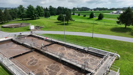 aerial tilt up of industrial american sewage treatment plant in lititz,pennsylvania. sunny day with green grass in suburb district. brown water in pool