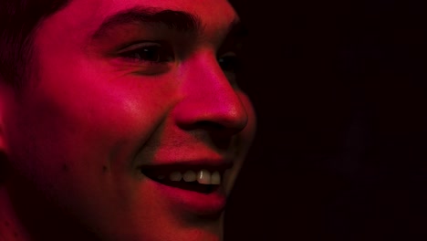 hombre sonríe y ríe en una habitación oscura iluminada por una pantalla en rojo