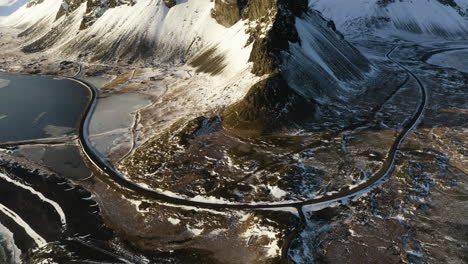 aerial tilt shot of a car driving on a coastal road, winter sunset in iceland