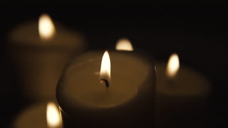 slow movement over burning candles, composition on black background, candles of different sizes stand side by side, slow motion