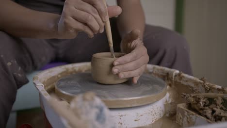 skilful craftsman concentrates cutting clay pot on turntable with ribbon tool slow motion