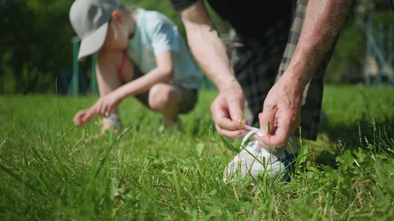 잔디 에 신발을 고 있는 노인의 클로즈업, 배경에 작은 아이가 잔디를 부드럽게 만지는 흐릿한 시각