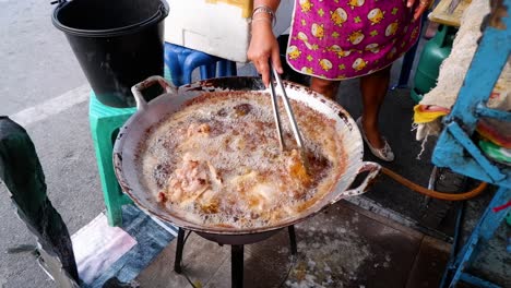 vendor frying chicken in hot oil outdoors