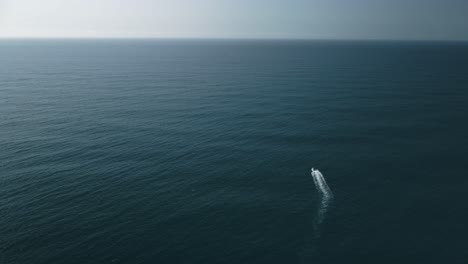 Toma-Aérea-De-Un-Pequeño-Barco-Solo-En-El-Vasto-Océano-Bajo-La-Luz-Del-Sol