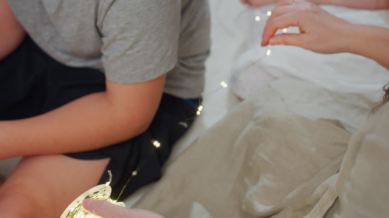 Partial view of mother and kids arranging Christmas lights. Boy in grey top and black shorts sits in front playing with dog, family enjoys holiday time together