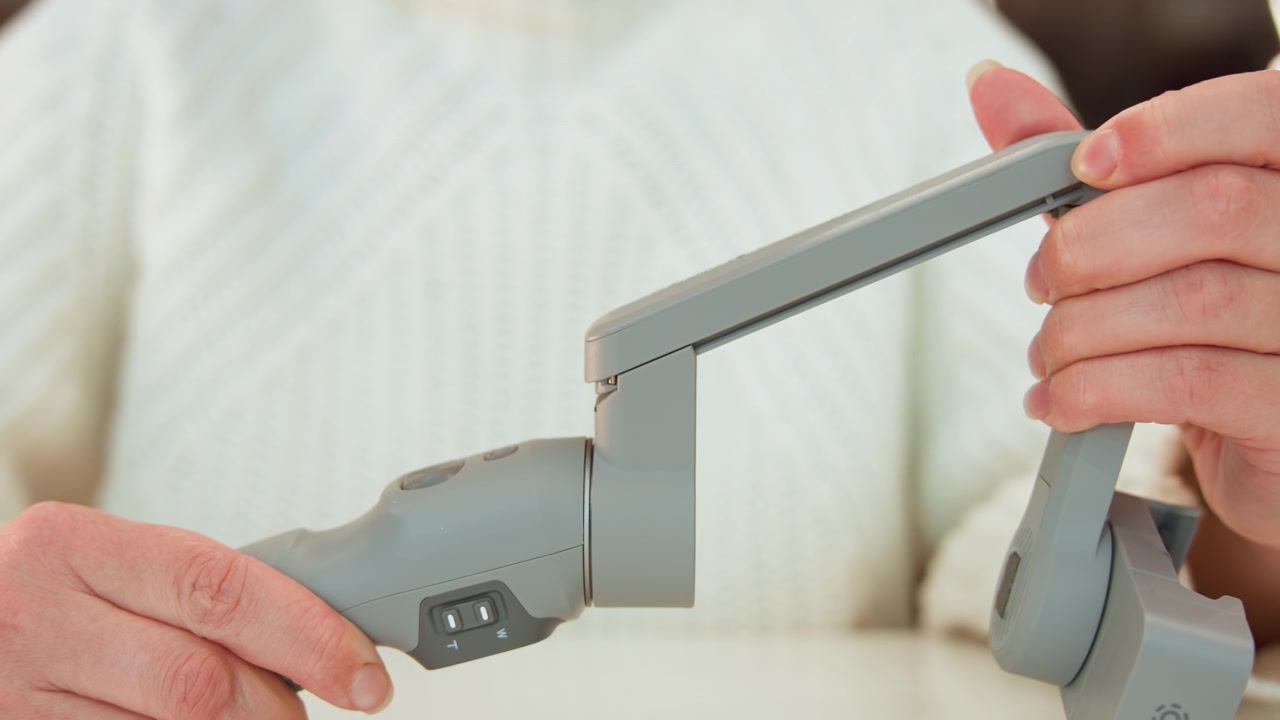 Close-up of hands unfolding portable gadget hinge, showing controlled rotation as top section lifts from base and creates visible gap; fingers grip edges and thumb applies pressure, emphasizing